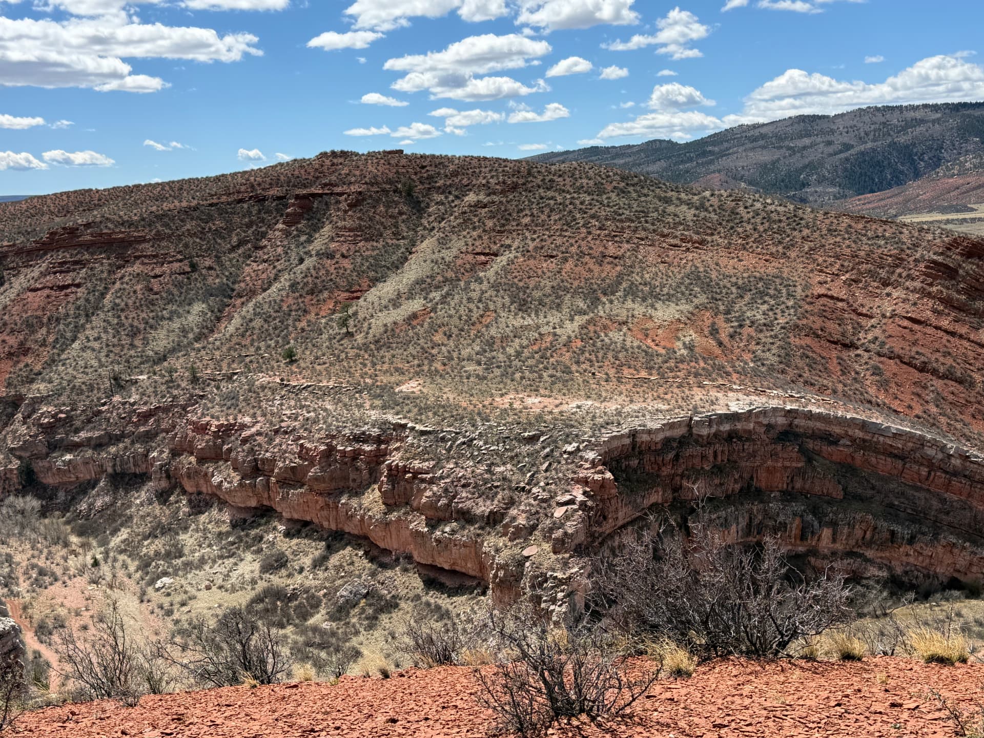 Exposed rock formations, layered ridgelines, and a deep desert canyon beneath a blue sky.