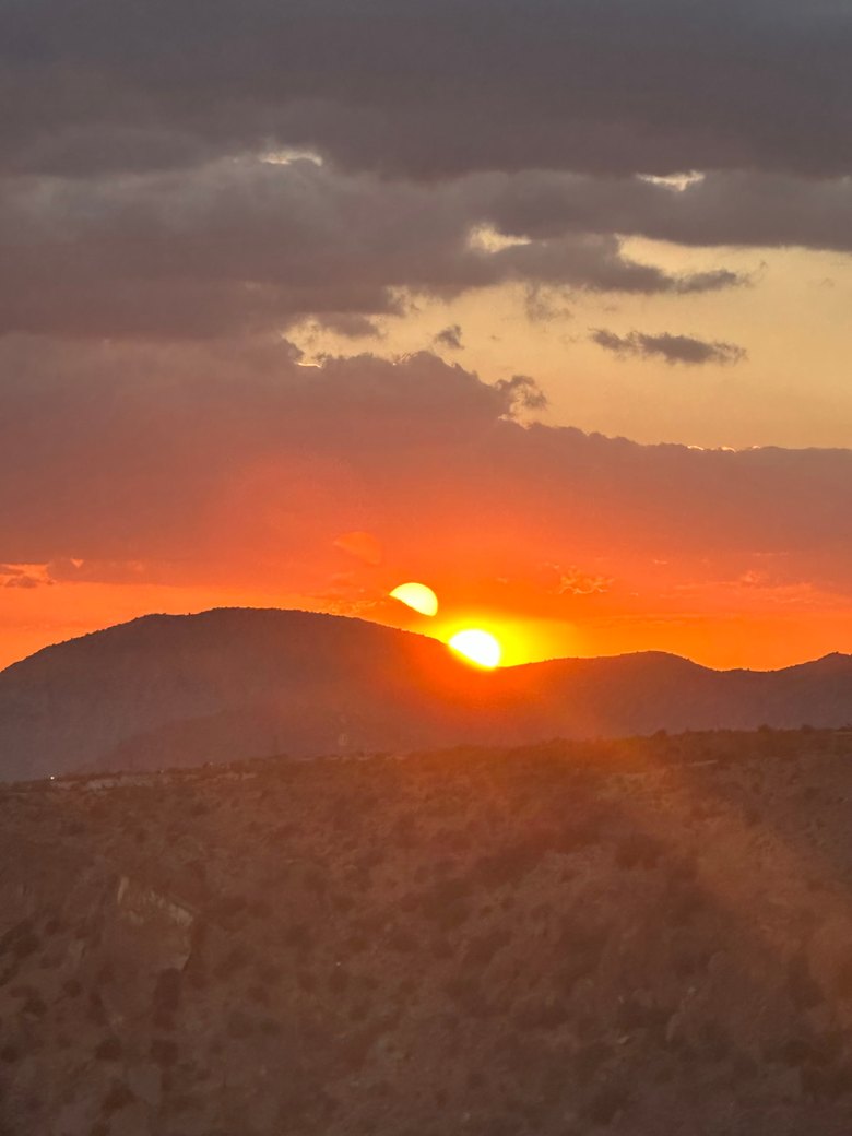 Sunset over a layered mountain ridgeline beneath dark clouds.